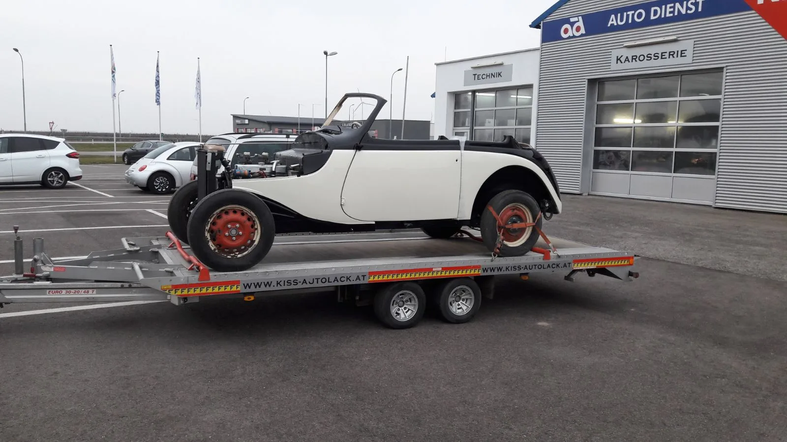 Restaurierter Oldtimer auf einem Anhänger vor der beschrifteten Werkstatt